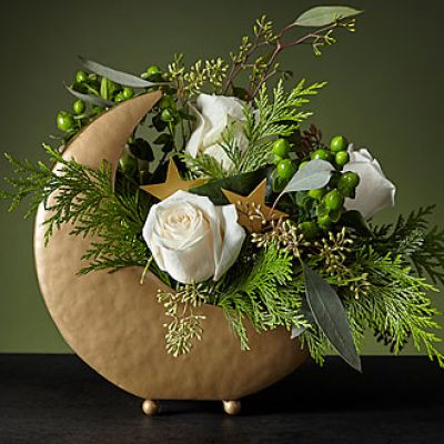 Drift off to visions of sugar plums under the Stardust Bouquet. This dreamy piece is arranged in a metal moon vase with stars nestled around the petals. Its white roses and delicate Christmas greenery will calm your space for a peaceful night.